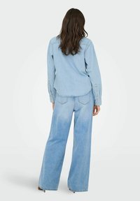 Jasnoniebieska koszula dżinsowa z zaokrąglonym dołem, długimi rękawami i mankietami na guziki; zestawiona z szerokimi jasnoniebieskimi dżinsami z tylnymi kieszeniami.