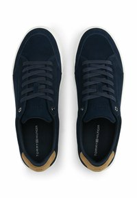Navy suede sneakers with a white rubber sole, featuring navy laces, a tan suede accent on the heel, and branded insole.