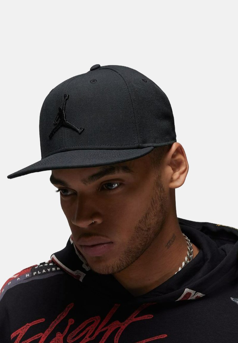 Sort baseball cap med flad skygge og broderet Jordan-logo. Materialet er solidt og tekstureret, med en struktureret form.