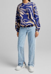 Blå och beige abstrakt mönster sweatshirt med rund halsringning, kombinerad med ljusblå vida jeans och vita plattformssneakers.