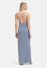 Długa, dopasowana, błyszcząca niebieska sukienka wieczorowa z niskim plecami i krzyżującymi się ramiączkami. Tkanina ma gładką teksturę i subtelny połysk.
