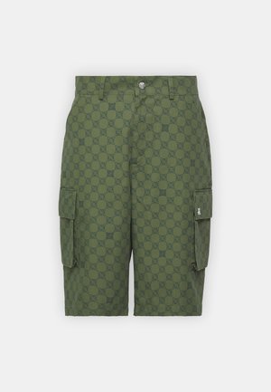 Zöld cargo short, textúrált mintával, nagy oldzsebekkel, gombos és cipzáras záródással, fehér sportcipővel.