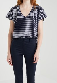 Marineblauwe en witte gestreepte blouse met korte mouwen en V-hals, gemaakt van zachte stof, gecombineerd met strakke marineblauwe trousers, met een ontspannen look.