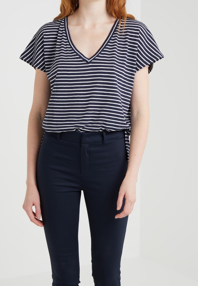 Marineblauwe en witte gestreepte blouse met korte mouwen en V-hals, gemaakt van zachte stof, gecombineerd met strakke marineblauwe trousers, met een ontspannen look.