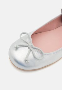 Bailarinas plateadas con acabado texturizado, punta redonda y un lazo trenzado como adorno. Interior de color rosa suave y suela marrón claro.