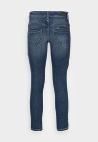 Jeans ajustados de mezclilla de color azul, con un lavado medio, dos bolsillos traseros con detalles de costura y un pequeño bolsillo con cremallera.