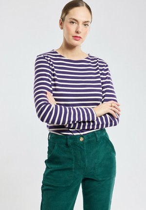 Haut à manches longues rayé en violet et crème, associé à un pantalon en velours côtelé vert avec un bouton à l'avant et des poches. Texture lisse, coupe décontractée.