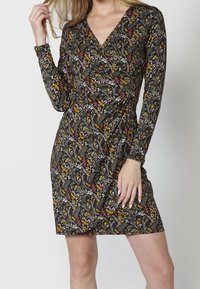 Sukienka z długim rękawem, charakteryzująca się czarną podstawą i misternymi kwiatowymi wzorami w kolorach czerwonym, żółtym i zielonym. Projekt z dekoltem w serek oraz dopasowanym krojem.