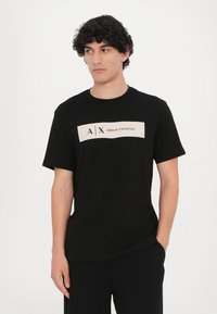 Svart bomull T-skjorte med en kremfarget grafikk av "A X ARMANI EXCHANGE" trykket på fronten, rund halslinning og korte ermer.