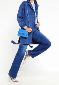 Niebieska dżinsowa kurtka na jasnoniebieskim swetrze, w połączeniu z szerokimi niebieskimi dżinsami i srebrnymi sneakersami. Mała niebieska torebka na ramię akcentuje outfit.