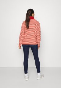 Suéter oversized em listras vermelhas e brancas com um alto colarinho, combinado com jeans skinny azul-escuro e ténis brancos. Design simples com um ajuste descontraído.