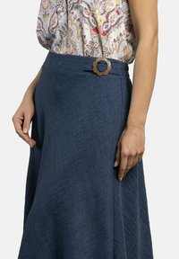 Falda de mezclilla en azul oscuro con una textura en la tela, presenta un botón de madera con diseño floral en la cintura y un corte fluido en A.