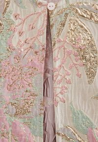 Blīvi šūts audums ar metālisku zelta pavedienu, rozā ziedu rakstiem, gaiši zaļām lapām un vienu baltu pogu, kas savieno divas plāksnes.