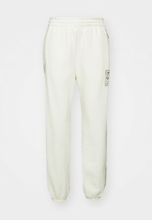 Lys beige joggebukser med elastisk midje, sidelommer og ribbestrikkede hem. Har et grafisk logo på venstre lår.