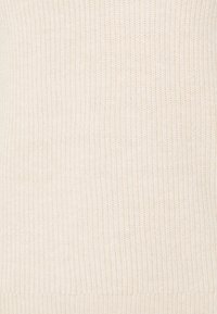 Gros plan sur un tissu tricoté beige avec une texture côtelée et une section de bordure festonnée en haut.