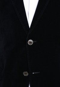 Svart sammet blazer med slagkrage, tvåknapplikning och subtila sömdetaljer. Inkluderar även en vit skjorta under.