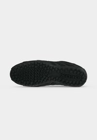 Semelle de chaussure noire avec des motifs circulaires antidérapants et le nom de la marque Geox embossé près du talon, présenté sur un fond clair uni.