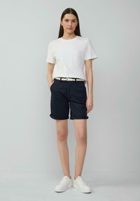 T-shirt en coton blanc, shorts bleus marine à revers et baskets blanches. Comprend une légère ceinture tressée. Design simple et décontracté.