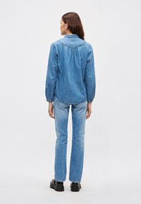 Denimbluse med rundet krage, lange puffede ermer og lett rynket rygg. Kombinert med lyseblå jeans med rette ben og platåsko.