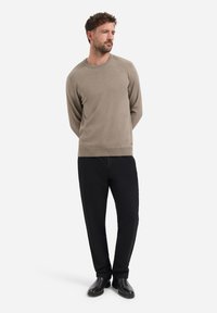 Lichtbruin gebreid trui met een ronde hals, textuurdetails op de schouders, gecombineerd met zwarte broek en zwarte schoenen.