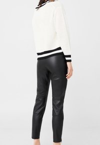 Biały sweter dziergany z czarnymi paskami na dekolcie i mankietach, w zestawie z czarnymi skórzanymi legginsami o gładkiej teksturze.