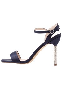 Námořnické modré sandály na podpatku s saténovým povrchem, disponující skládací špičkovou páskou a ozdobným krystalovým blokovým podpatkem. Součástí je nastavitelné páskové zapínání na kotníku.