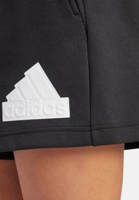 Shorts deportivos negros que presentan un prominente logo blanco de Adidas en un diseño texturizado, con un acabado de tela suave y bolsillos laterales.