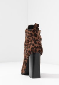 Bottine à imprimé léopard marron et noir avec un talon noir haut et épais, vue de dos sur une surface blanche.