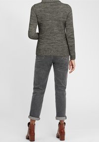 Grauer Strickpullover mit hohem Kragen, kombiniert mit hochgekrempelten grauen Hosen und braunen Stiefeletten. Die Textur ist weich und lässig.
