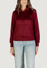 Felpa con cappuccio bordeaux dal taglio dritto, con tasca a marsupio frontale e polsini a costine, abbinata a jeans azzurri chiari con un motivo logo.