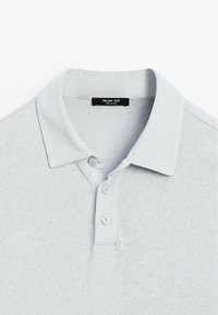 Světle šedá polo tričko s měkkou textura, dvěma knoflíky a klasickým límcem. Štítek uvádí "Massimo Dutti, Vyrobeno v Číně."