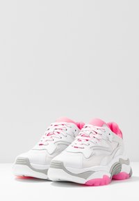 Baskets blanches et grises avec des accents roses, composées de matériaux en mesh et synthétiques. Semelle épaisse, bout arrondi et lacets contrastés.