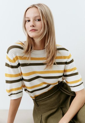 Strickpullover mit horizontalen Streifen in Gelb, Olivgrün und Weiß; hat einen runden Ausschnitt und kurze Ärmel. Getragen mit hochgeschnittenen Hosen.