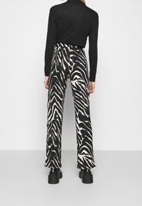 Breda byxor med ett svart och vitt zebramönster, tillverkade av strukturerad tyg. Avslutade med hög midja och bärs med svarta skor.