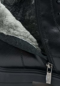 Černá kožená bota s šedým, chlupatým podšívkou a podrobností se zipem. Interiér má jemnou strukturu a pevnou podrážku.