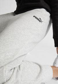 Šedé tepláky s texturovaným povrchem, na boku s výrazným černým logem Puma. Pohodlný střih s zúženým designem nohavic.