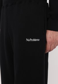 Schwarze Baumwoll-Sweatpants mit gerippten Bündchen und einem weißen gestickten "No Problemo"-Logo auf dem linken Oberschenkel.
