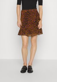 Ruskea leopardi-kuvioinen hame, jossa on pinkkejä yksityiskohtia, röyhelöinen helma, kevyt kangas ja istuva vyötärö. Päällä mustat loaferit.