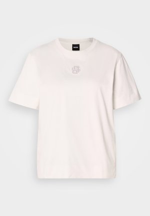 Biała kokvilnas T-krekls ar apaļu izgriezumu, īsām piedurknēm un smalku logo detaļu centrā, kurā ir mazi metāliski sukņi.