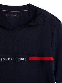 Tengerészkék, rövid ujjú póló, puha anyagból készült, kerek nyakkivágással, piros díszcsíkkal és fehér színű "TOMMY HILFIGER" logóval.