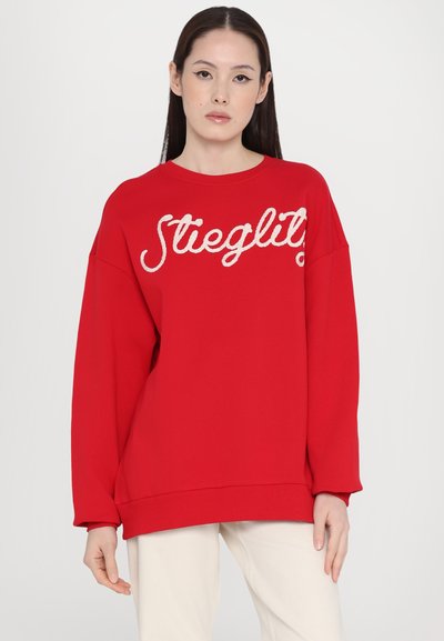 Sudadera roja de gran tamaño, hecha de tejido de punto, con el texto bordado en blanco "Stieglitz" en la parte delantera, y puños y dobladillo acanalados.
