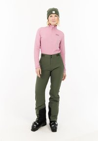 Lichtroze zip-up lang mouwtop, groene sneeuwbroeken met zwarte onderaccenten, zwarte skibotten. Eenvoudig, aansluitend ontwerp geschikt voor wintersport.