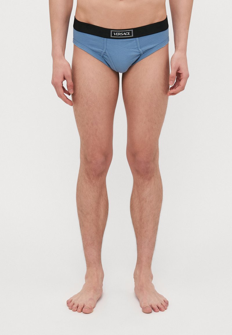 Culottes en coton bleu avec une ceinture élastique noire affichant le logo "VERSACE". Le design comprend une poche profilée et une coupe ajustée.