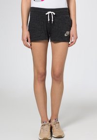 Šedé Nike šortky s bílým stahováním, předními kapsami a logem. V kombinaci s béžovými teniskami, které mají texturovaný svršek a šňůrky.