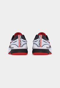 Ζευγάρι αθλητικά παπούτσια Reebok σε λευκό, μαύρο και κόκκινο χρώμα, εμφανιζόμενα από πίσω, με κόκκινες κάθετες ρίγες και μαύρες μεσαίες σόλες.