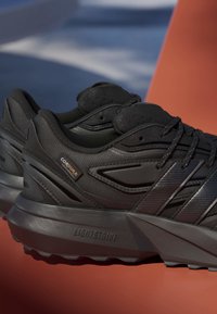 Čierne športové topánky vyrobené z textúrovaných syntetických materiálov, s masívnou podrážkou s brandingom "LIGHTSTRIKE" a akcentmi z Cordura.