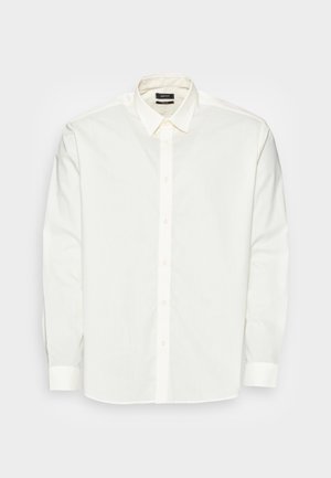 Camisa de vestir blanca de manga larga con botones en la parte delantera y cuello puntiagudo, colocada sobre una superficie clara.