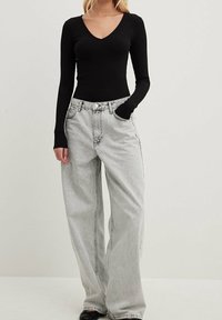 Černý žebrovaný top s dlouhým rukávem a výstřihem do V, v kombinaci se světle šedými širokými džíny. Oblečení má jemné švy a volný střih.