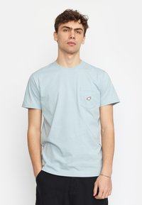 Lichtblauwe katoenen T-shirt met ronde hals, korte mouwen en een borstzak met een klein oranje en wit grafisch ontwerp.