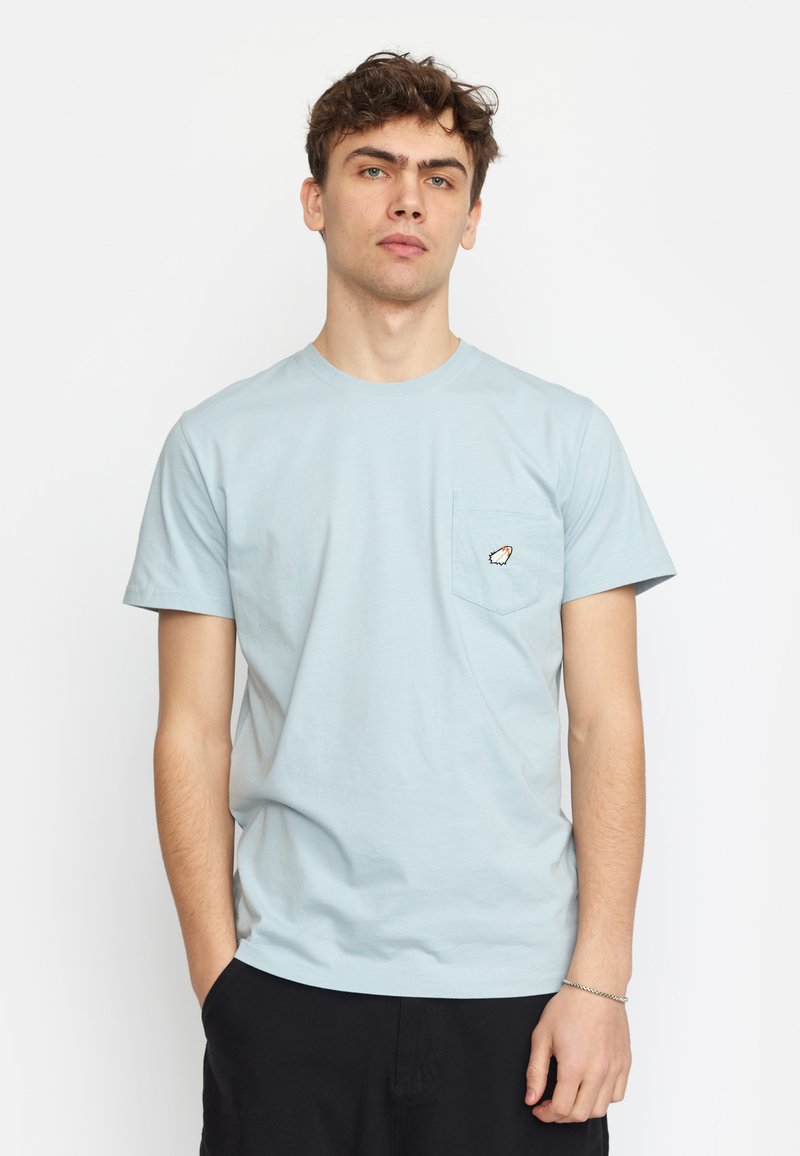 Lichtblauwe katoenen T-shirt met ronde hals, korte mouwen en een borstzak met een klein oranje en wit grafisch ontwerp.
